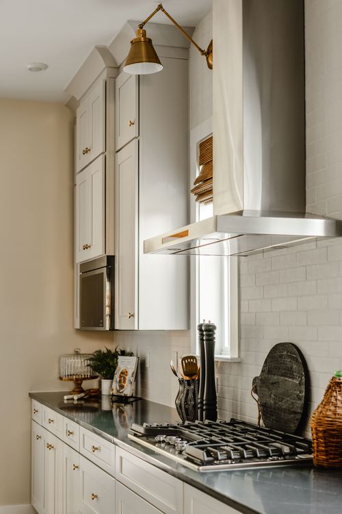 Kitchen cooktop detail with a brass sconce, stainless hood, and subway tile backsplash