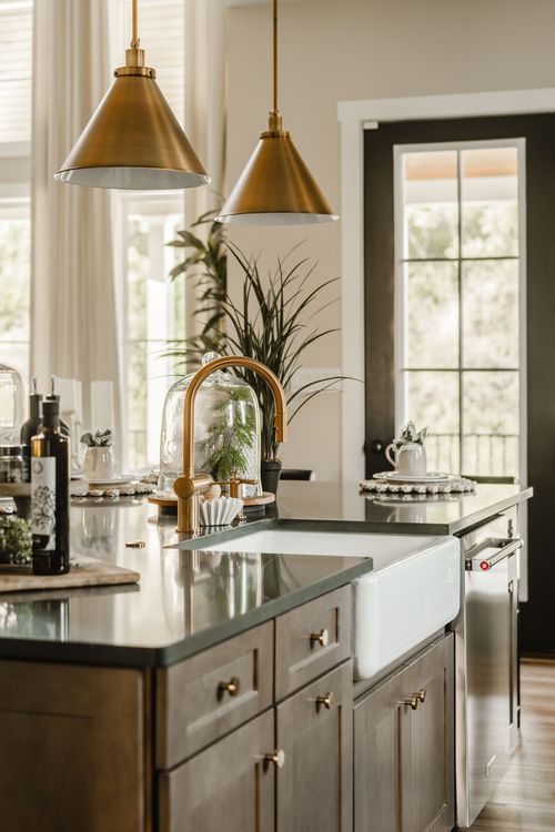 Kitchen island with a farmhouse sink, brass gooseneck faucet, and brass pendant lights
