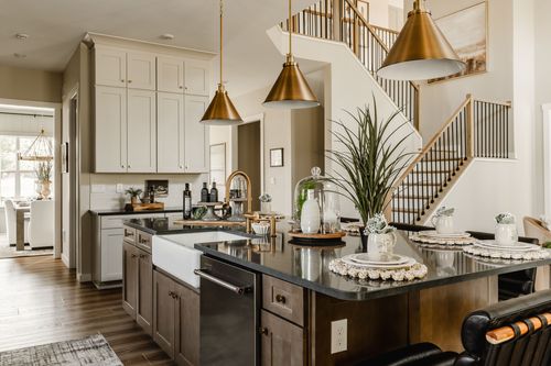 Kitchen island with a farmhouse sink and gold fixtures beneath brass pendants, staircase beyond