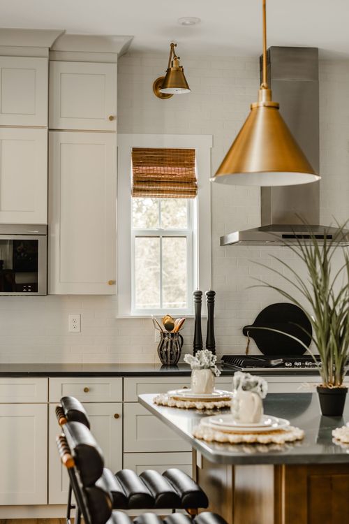 White kitchen with brass pendant lighting, black island countertop and leather barstools