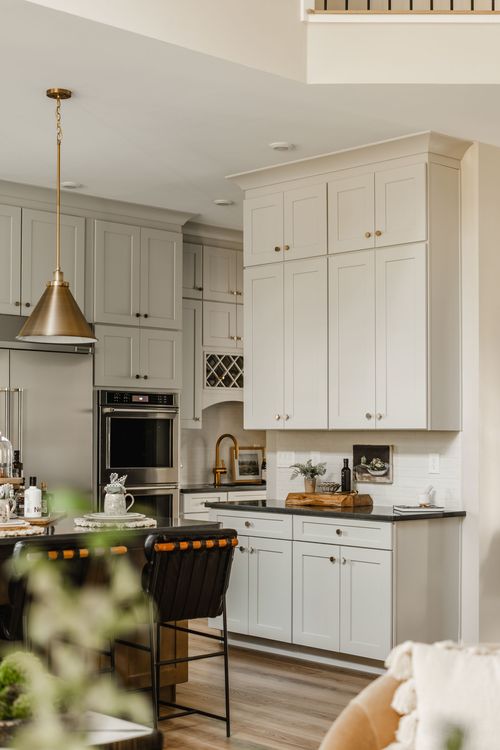 Open kitchen with sage cabinetry, black countertops and a brass pendant over the island