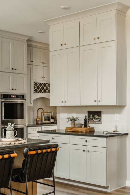 Kitchen with tall cream cabinetry, black countertops and a lattice-front wine rack nook