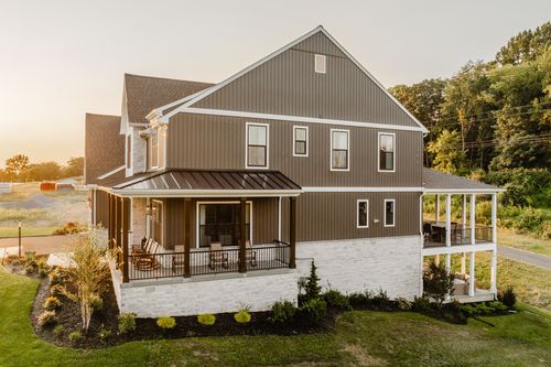 Rear exterior of a farmhouse with a covered porch, stone base, and rolling countryside views at sunset