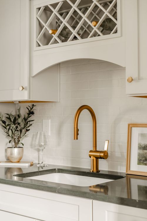 Close-up of a lattice wine rack cabinet above a brass faucet and marble tile