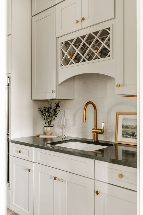 Bar sink area with a brass faucet, wine storage cabinet and framed art on marble tile