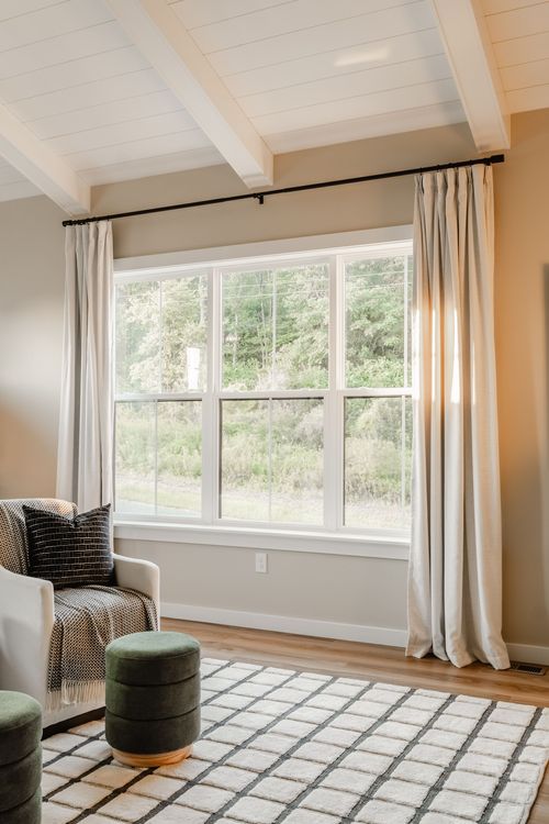Sitting nook with vaulted shiplap ceiling, tall window, cream armchair and green ottomans
