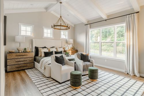 Primary bedroom with cream upholstered bed, wagon-wheel chandelier and plaid rug in Lititz, PA
