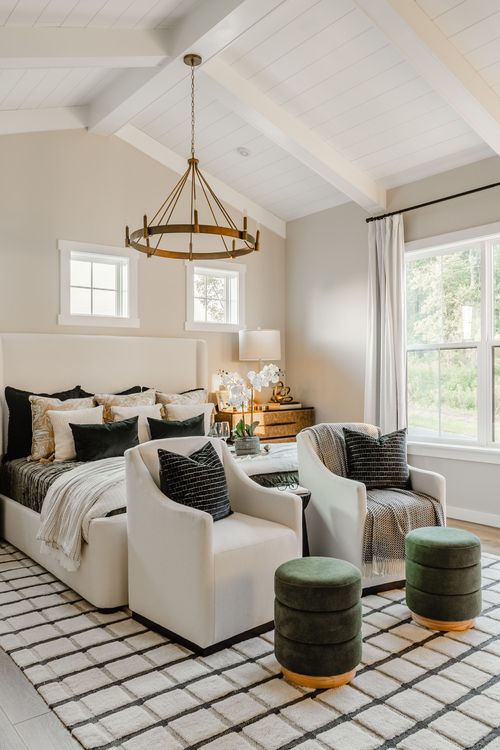 Primary bedroom with cream accent chairs, black throw pillows and green velvet ottomans