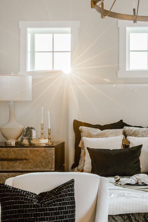 Sunlit bedroom nightstand with brass candlesticks, a table lamp and black velvet pillow