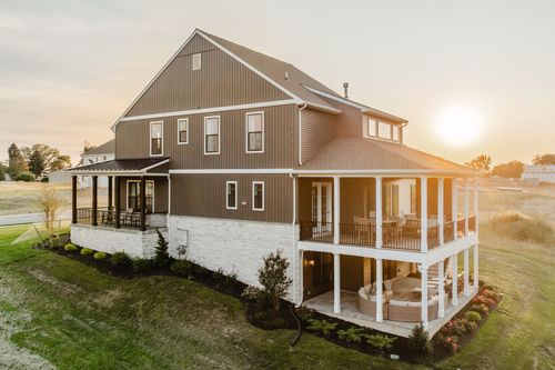 Aerial rear view of a farmhouse with a wraparound porch and stone patio at sunset