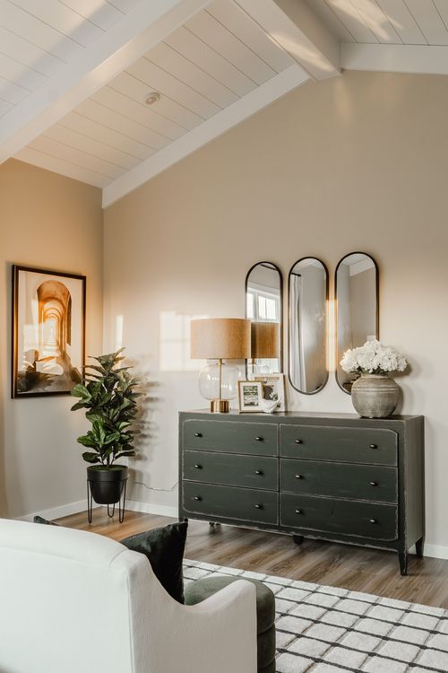 Bedroom corner with a dark green dresser, arched mirrors, potted plant and framed art