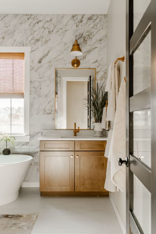 Primary bathroom with a marble slab wall, freestanding soaking tub and wood vanity