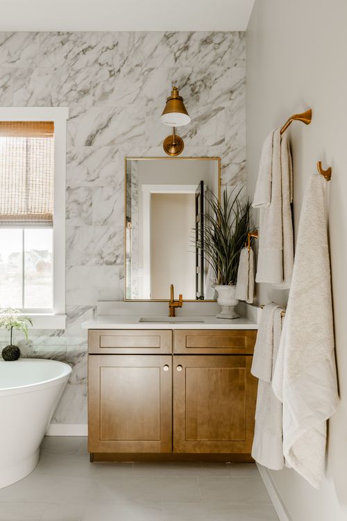 Bathroom vanity with wood cabinetry, marble tile wall, brass sconce and hanging towels