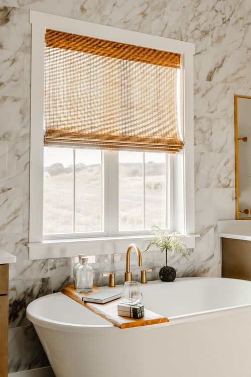Bathtub set beneath a bamboo shade window, styled with a wood tray and amenities