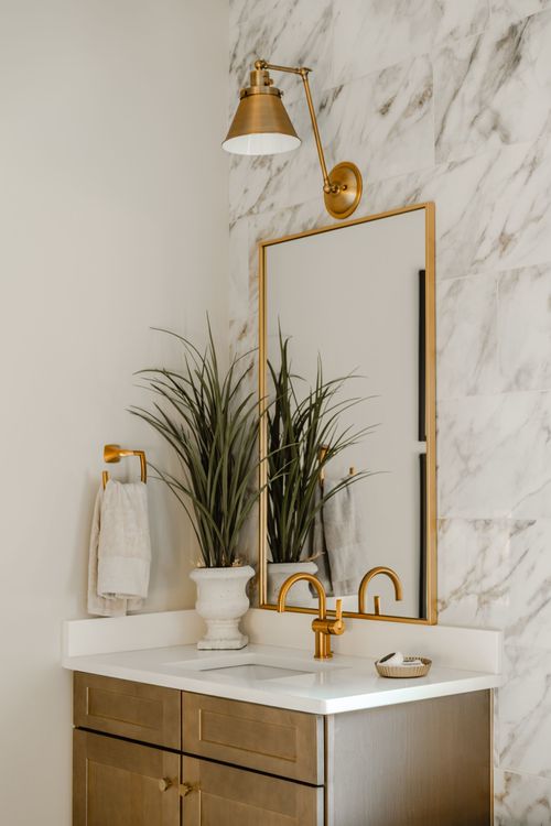 Powder room vanity with brass sconce, arched mirror, gold faucet and marble tile wall