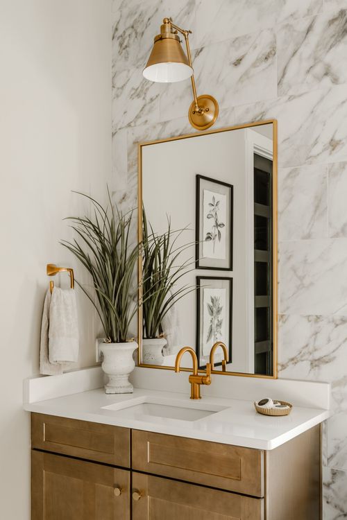 Powder room vanity with marble tile, gold fixtures, framed botanical prints and a plant
