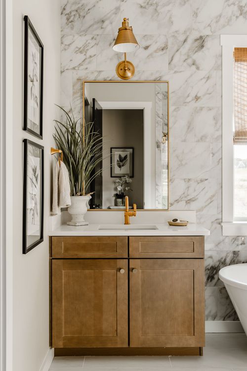 Powder room with a wood vanity, marble tile wall, gold sconce and botanical art