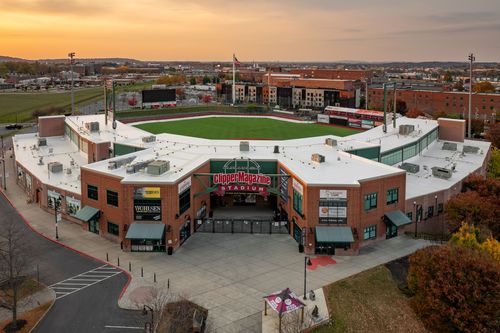 Aerial view of a covered stadium grandstand at golden-hour sunset above a city skyline