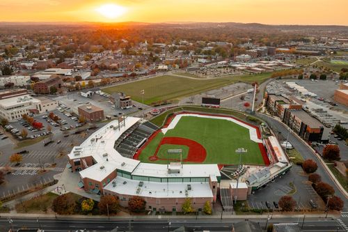 Aerial sunset view of a minor league ballpark with a curved canopy roof and city skyline