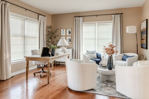 White-toned home office and sitting area with a wood desk, sheer curtains and hardwood floors