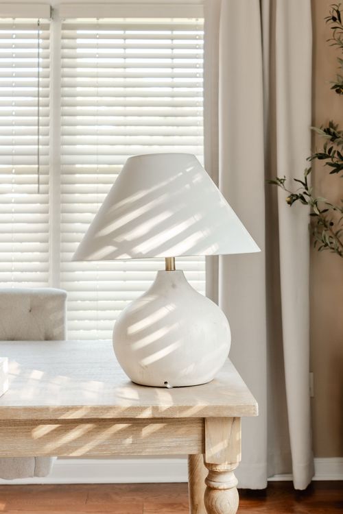 Close-up of a white swirled ceramic table lamp beside a window with sheer curtains