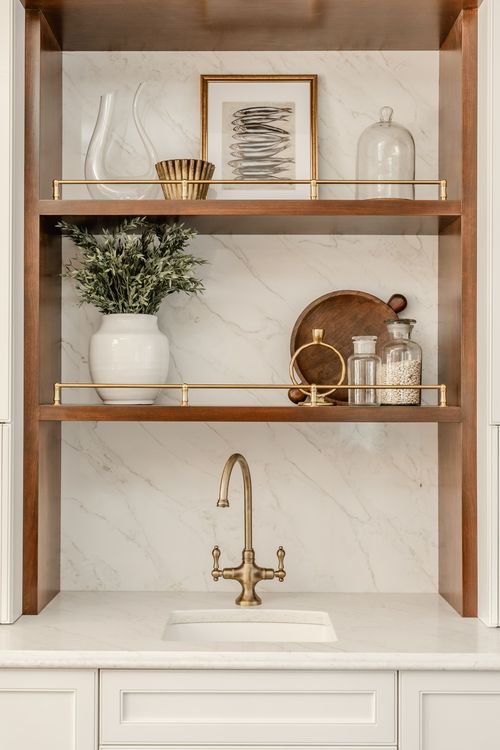 Wood bar niche with open shelving styled with a decanter, framed art and a brass sink faucet