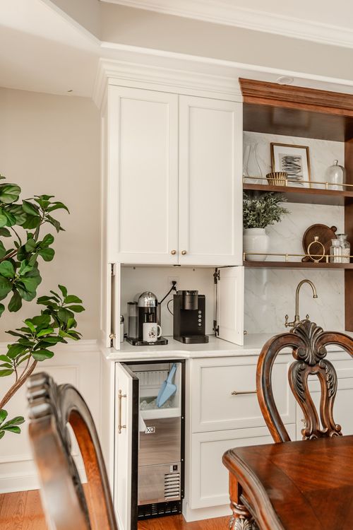 Coffee bar nook with a built-in ice maker and espresso machine behind folding cabinet doors