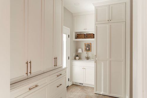 Butler's pantry hallway with brass-pulled cabinets, a small sink nook and tile floor
