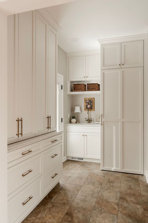 Tall white pantry cabinetry beside a mudroom sink nook with woven storage baskets