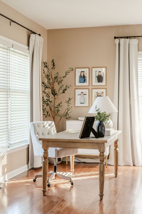 Home office with a wood desk, tufted white chair and a family photo gallery wall