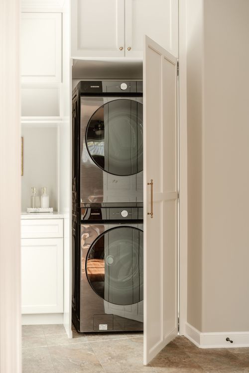 Stacked black stainless washer and dryer tucked behind a paneled cabinet door