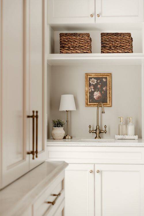 Small utility sink with a brass faucet, framed floral art and woven baskets on open shelving