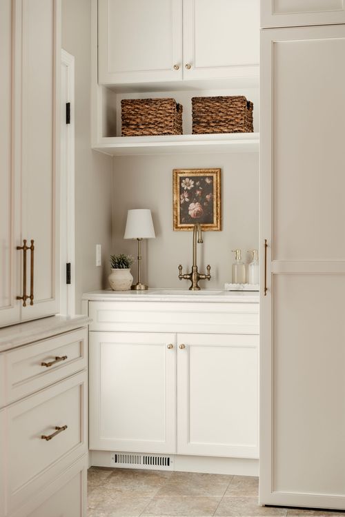 Butler's sink nook with brass faucet, a table lamp and woven baskets between white cabinetry
