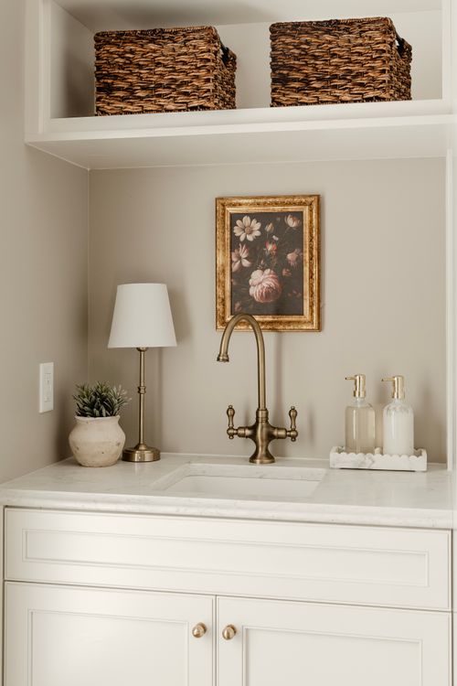 Marble sink nook with brass faucet, table lamp, potted succulent and framed floral print