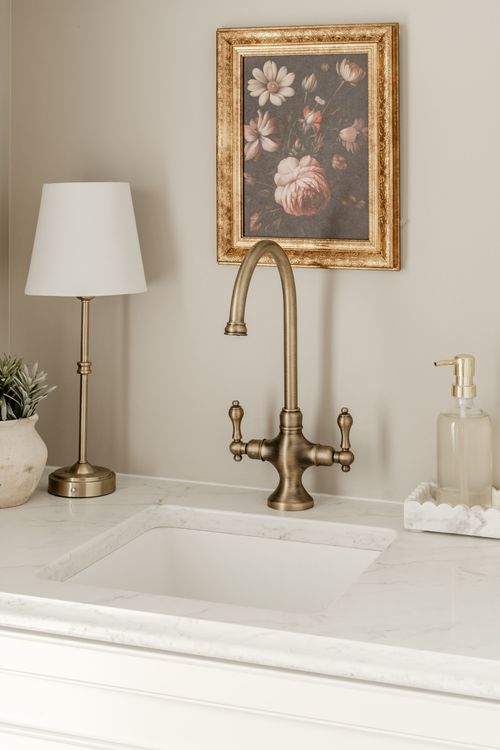 Close-up of a brass gooseneck faucet and framed floral art above a marble sink