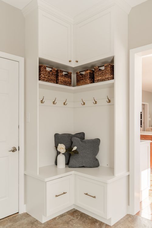 Corner mudroom bench with brass coat hooks, woven baskets and gray throw pillows