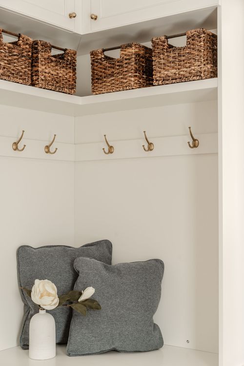 Mudroom bench detail with brass hooks, woven storage baskets and a magnolia stem in a vase
