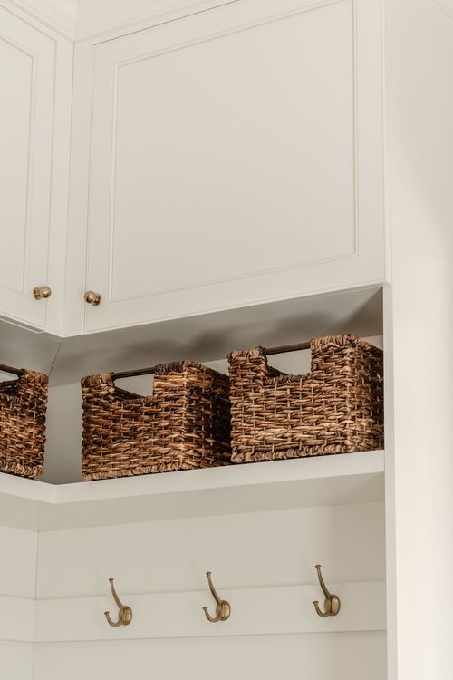 Detail of woven baskets and brass coat hooks on white mudroom shelving