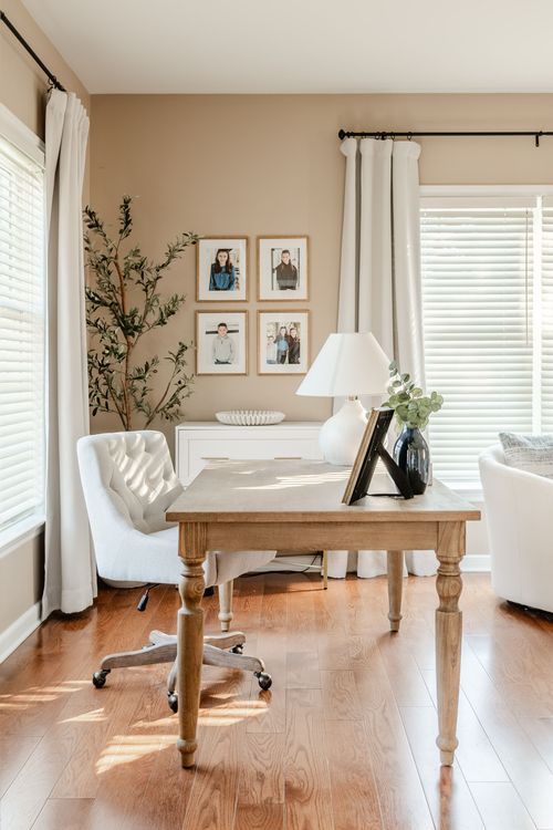 Home office with a wood desk, tufted chair, faux olive tree and gallery wall photos