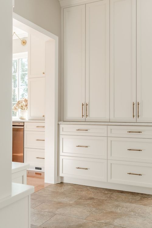 Hallway with built-in cabinetry and brass pulls opening into a kitchen with tile flooring