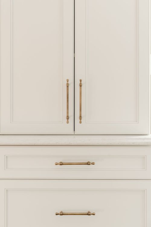 Close-up of long brass bar pulls on white cabinet doors and drawers