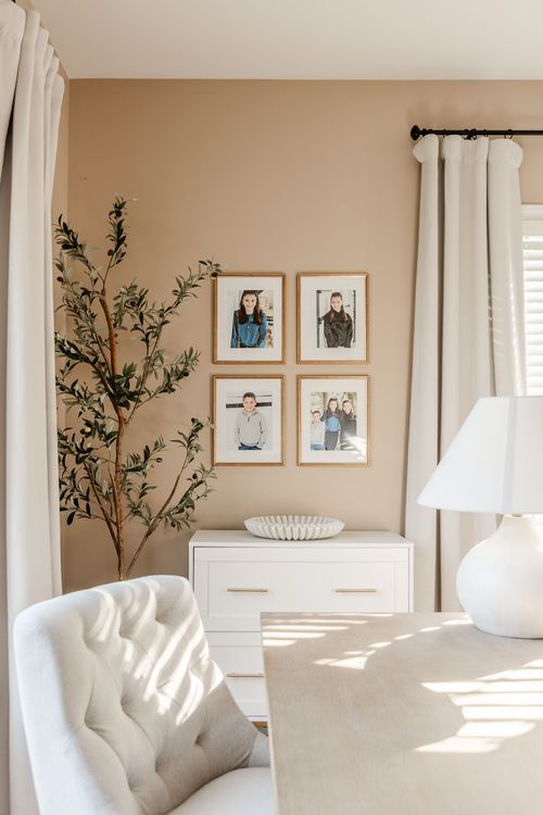 Family photo gallery wall above a white dresser beside a tufted chair and desk
