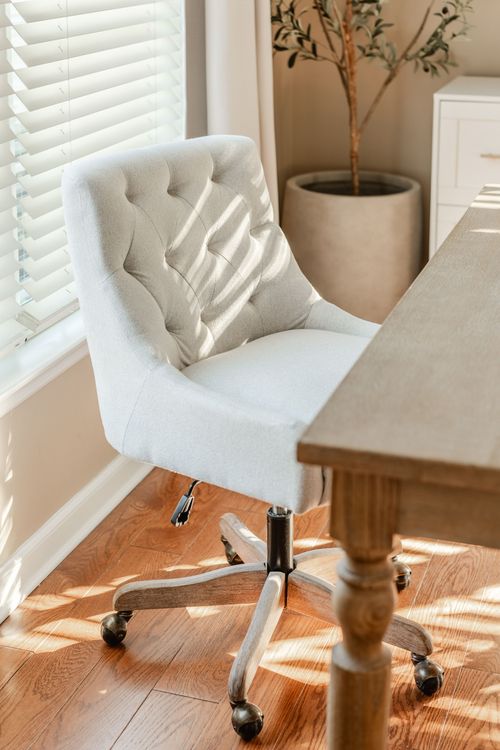 Close-up of a white tufted swivel office chair beside a wood desk