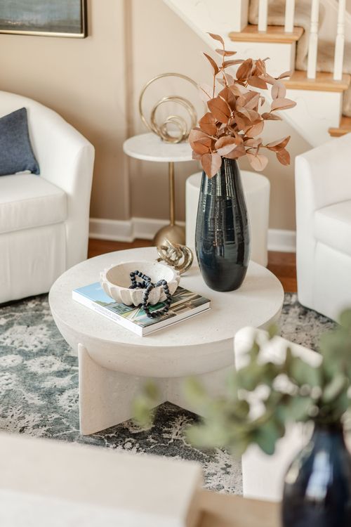 Round white coffee table with a gold knot sculpture, black vase and staircase behind