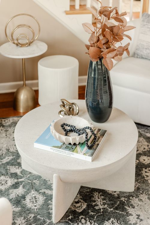 Coffee table detail with a marble bowl, beaded bracelet and a magazine beside a dark vase
