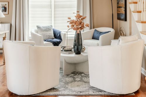 Four white swivel chairs around a round coffee table with a dark vase and patterned rug
