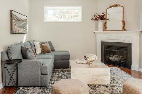 Living room with a gray sectional, cream ottomans and a white mantel fireplace