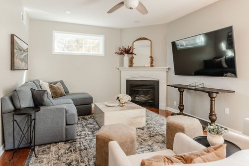 Living room with a gray sectional, corner fireplace and cream chairs on a patterned rug