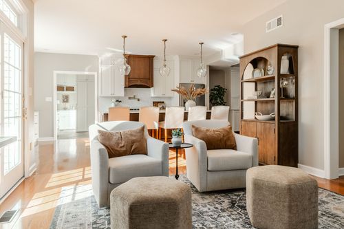 Open kitchen and sitting area with glass pendant lights, cream armchairs and a wood hutch