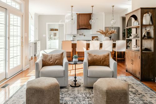 Kitchen with glass pendant lighting and wood cabinetry seen past two cream armchairs